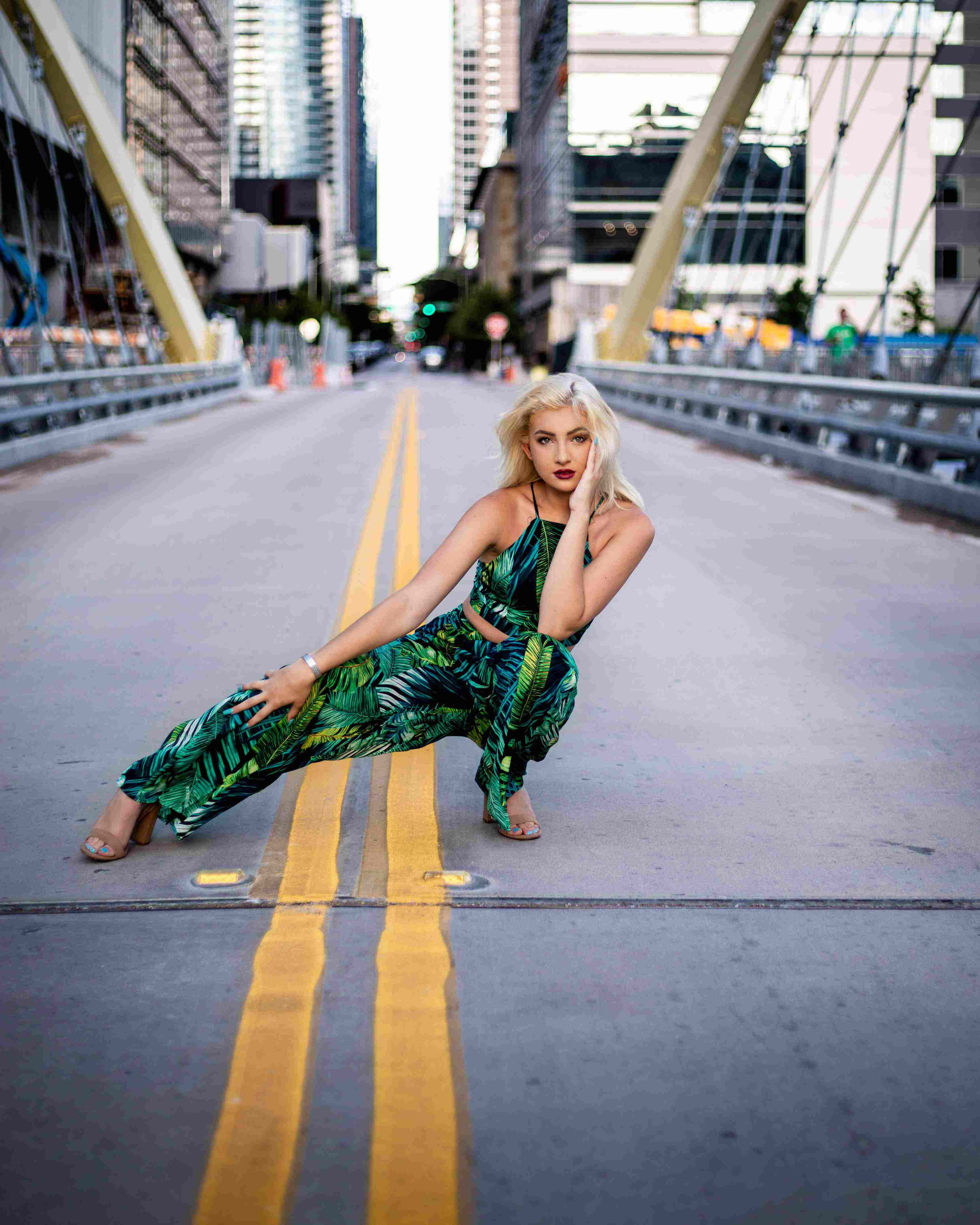 picture, woman in a green botanical print outfit posing on a city bridge